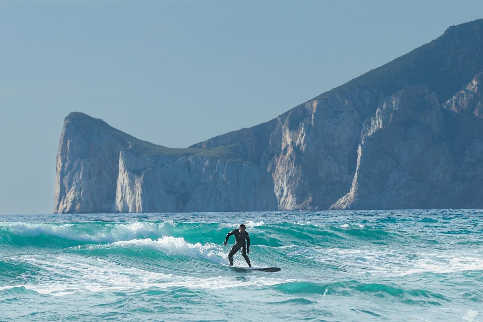 Een surfer die een golf pakt met een hoge klif op de achtergrond.