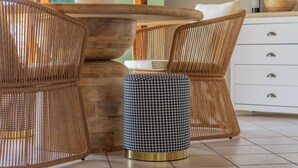 Un comedor con sillas de mimbre, una mesa redonda y un otoman estampado.