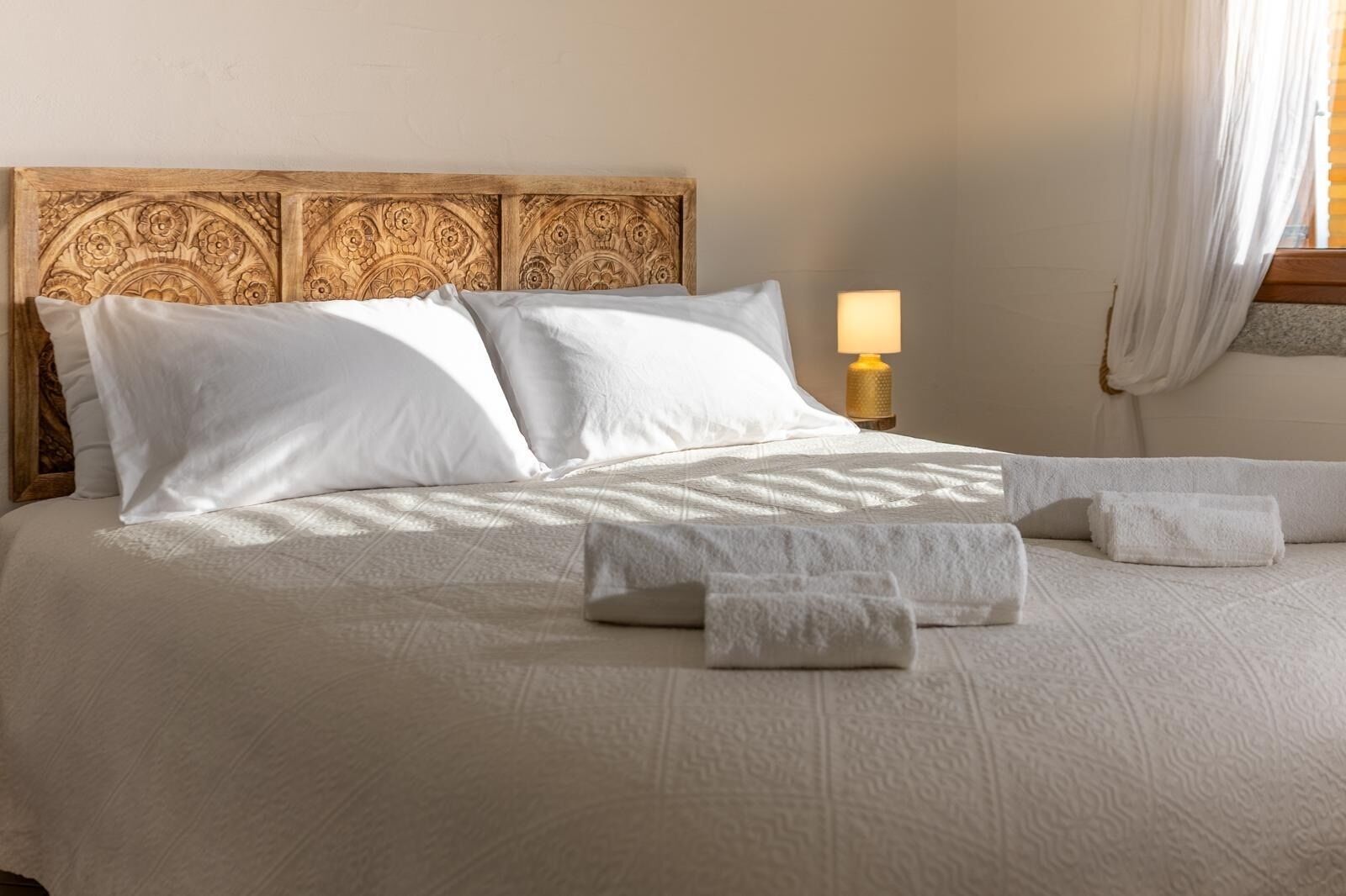Un lit bien fait, avec du linge de lit blanc, une tête de lit en bois ornée de motifs complexes et une lampe de chevet.