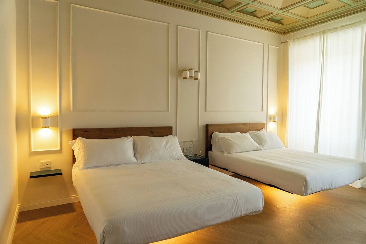 A hotel room with two beds, a wooden headboard, a nightstand, and wall-mounted lamps.