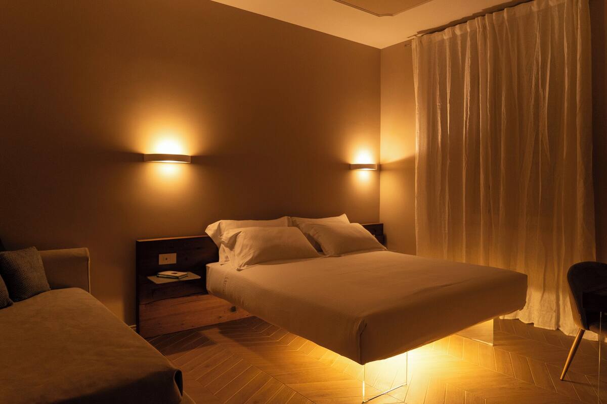 A hotel room with a bed, a nightstand, a chair, and two wall-mounted lights.