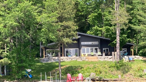 Un chalet au bord du lac, doté d’un quai, et entouré d’une forêt dense.