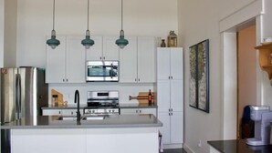 Une cuisine moderne avec des meubles blancs, un îlot central, des appareils en acier inoxydable et des luminaires suspendus.