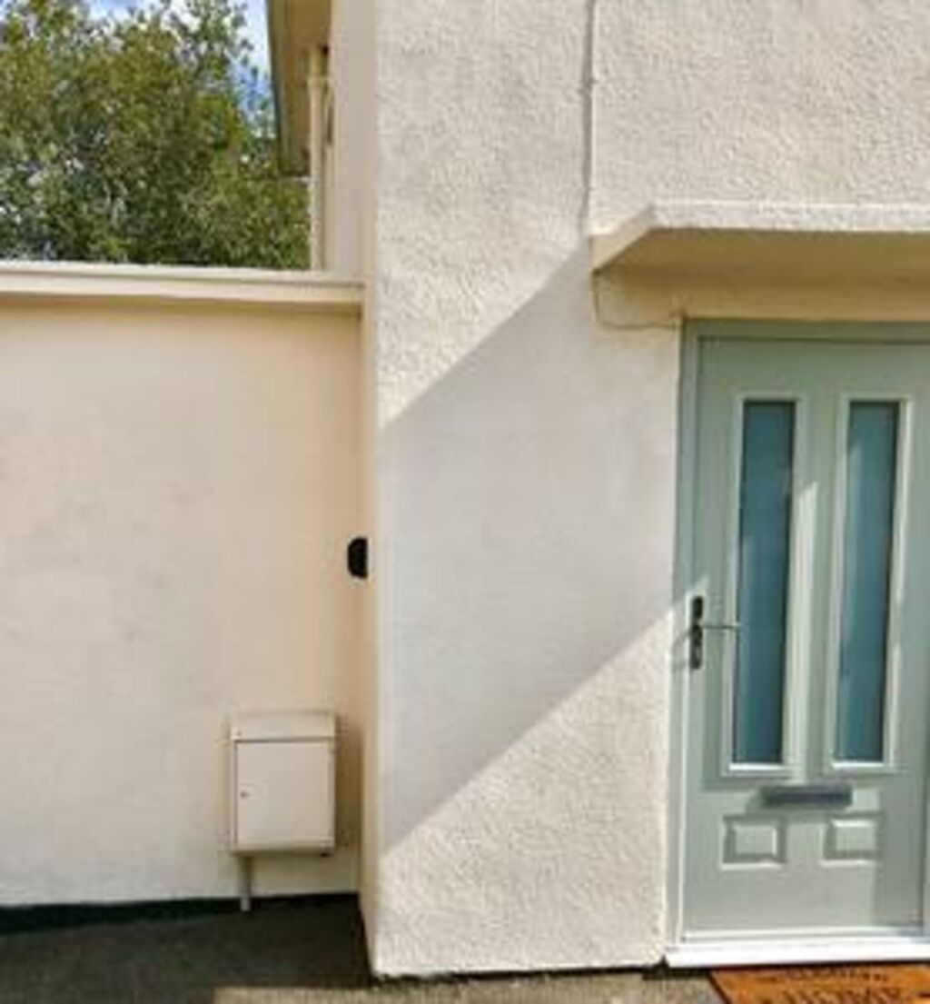 A white exterior wall with a small electrical box and a light blue door with a window.