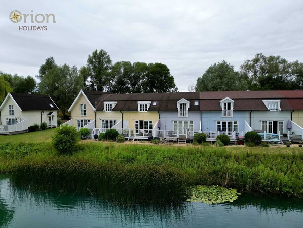 A row of colorful houses by a calm lake with a dock. - Isis Lakes 31, Bonheur - Lakeside Holiday Lodge, On-site Activities, Sleeps 6 (South Cerney)
