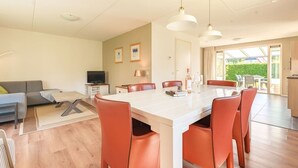 A modern kitchen with a central island, dining table, and chairs. There is a television, a lamp, and a bottle on the island.