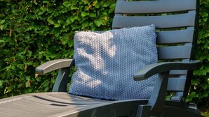 A dark-colored lounge chair with a textured cushion and a pair of sandals on the grass.