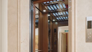 L’intérieur d’un ascenseur avec une porte en verre, une porte en bois et un plafond orné d’un motif en réseau.