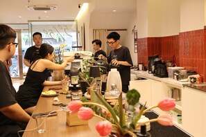 A modern kitchen with a coffee station, a dining table with people, and a view of the street outside. - Hanoi Ivory Hotel (Hanoi)