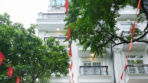 L’entrée de l’hôtel Hanoi Ivory, avec une voiture garée devant, un escalier menant à l’entrée et des drapeaux rouges suspendus au balcon.
