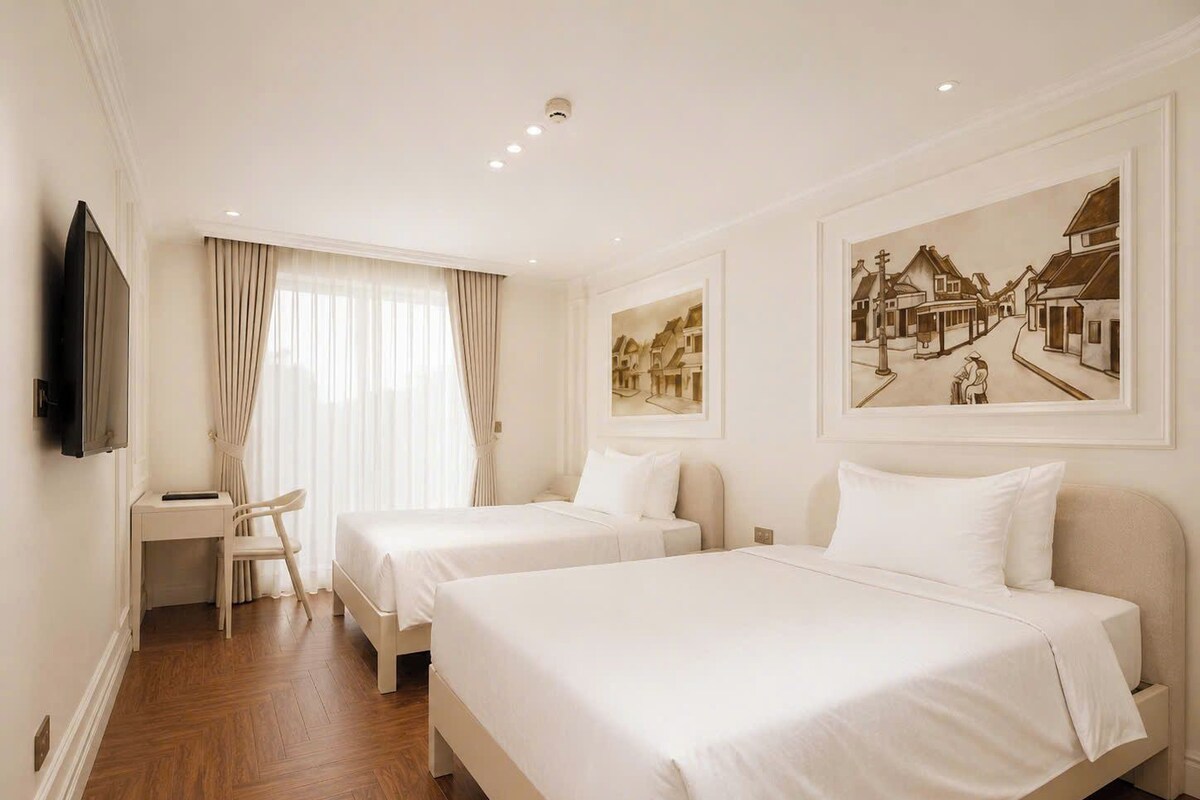 A hotel room with two beds, a desk, a chair, and artwork on the walls.