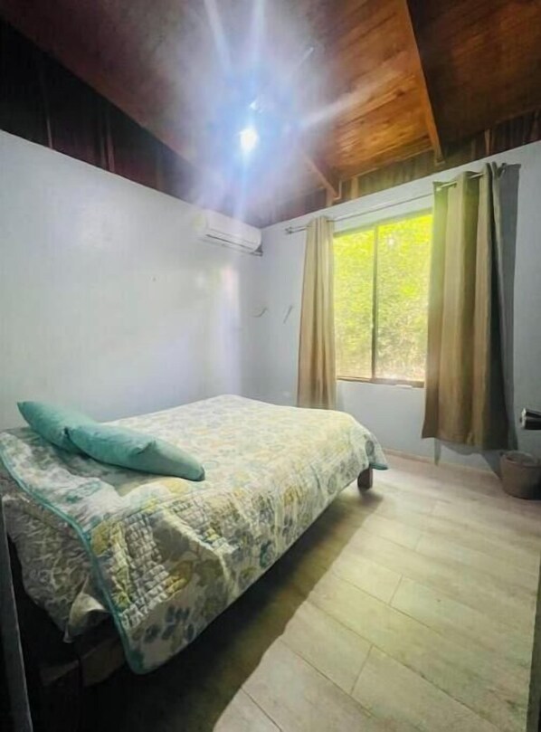 Une chambre à coucher avec un lit, une fenêtre avec des rideaux et un appareil de climatisation.