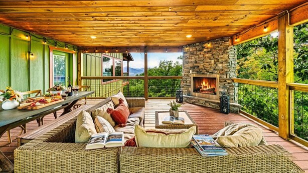 A cozy outdoor seating area with wicker furniture, a stone fireplace, and a view of the outdoors. - Swim in the Clouds - Luxe 6BR Cabin w/ Views & Pool (Pigeon Forge)
