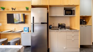 A compact hotel room with a kitchenette, a refrigerator, a microwave, and a small dining area with a table and chairs.