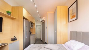 A compact hotel room with a bed, a kitchenette, and a small bathroom.