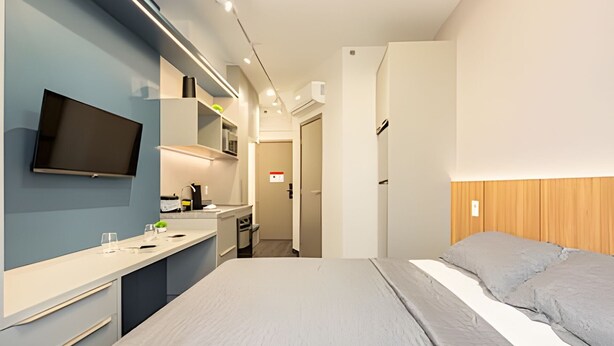 A modern hotel room with a bed, a TV, a kitchenette, and a bathroom. - Beautiful studio in São Caetano ap614 (São Caetano do Sul)