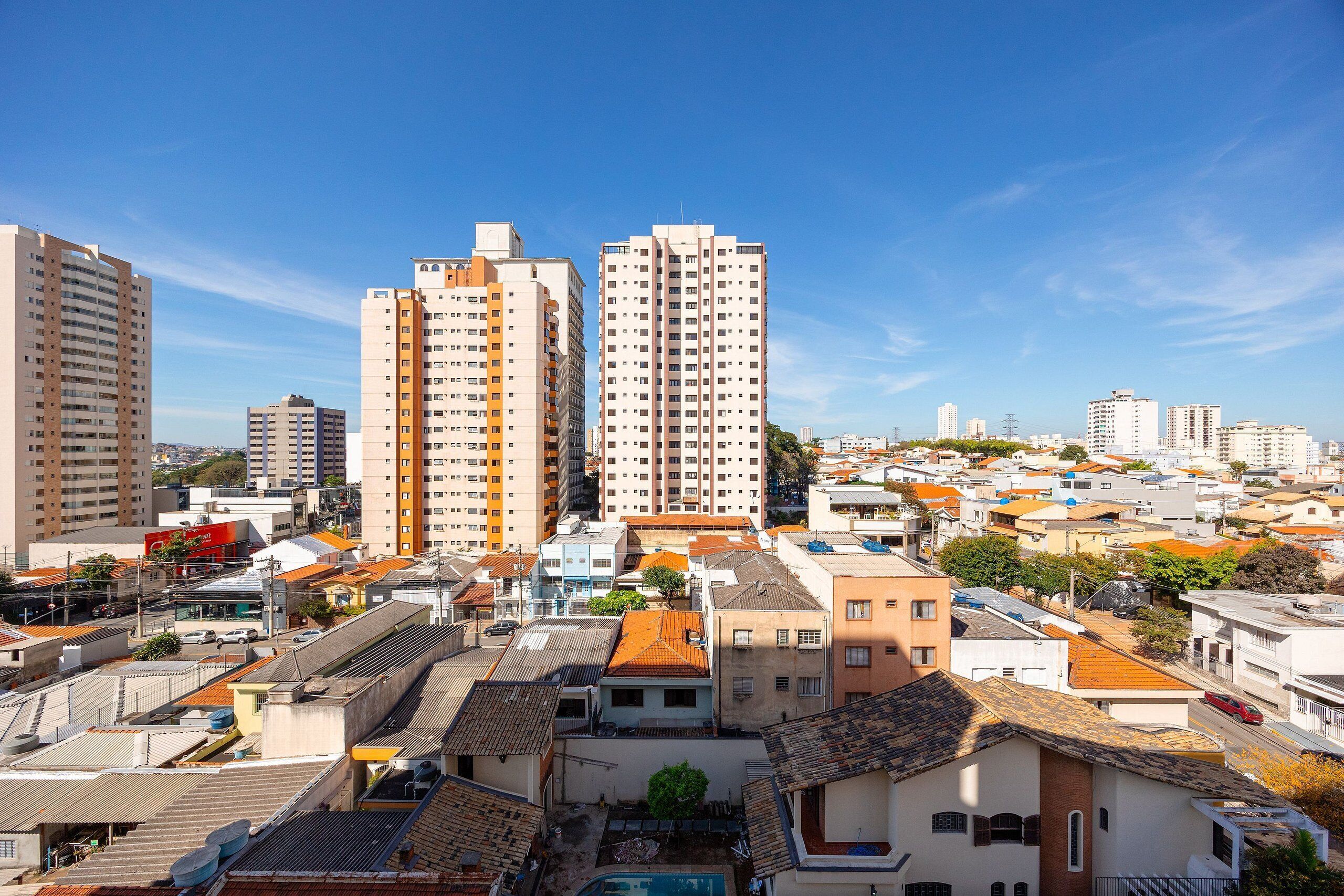 Un paysage urbain avec de hauts immeubles, un mélange de bâtiments résidentiels et commerciaux, et un ciel bleu dégagé.