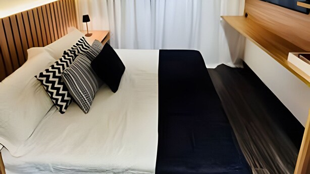 Et hotelværelse med en seng, bænk, fjernsyn og gardin.