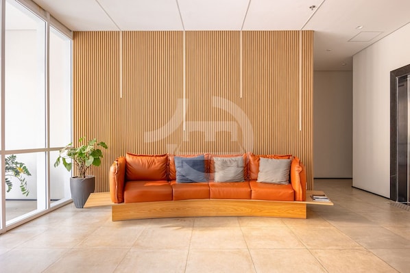 A modern interior with a curved orange leather sofa, a wooden slatted wall, and a potted plant.