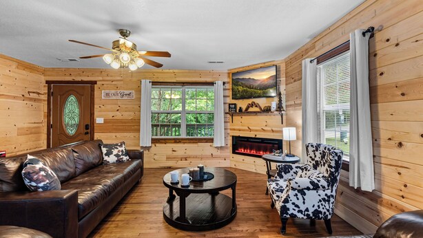 A cozy cabin interior with a leather sofa, a round coffee table, a patterned armchair, and a fireplace.