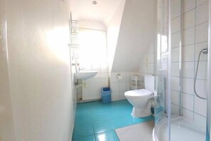 Ein Badezimmer mit Toilette, blauem Mülleimer, Duschkabine aus Glas und Waschbecken.