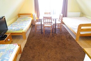 Ein Zimmer mit zwei Einzelbetten, einem kleinen Tisch mit Stühlen, einem Fernseher auf einem Schrank und einem braunen Teppich.