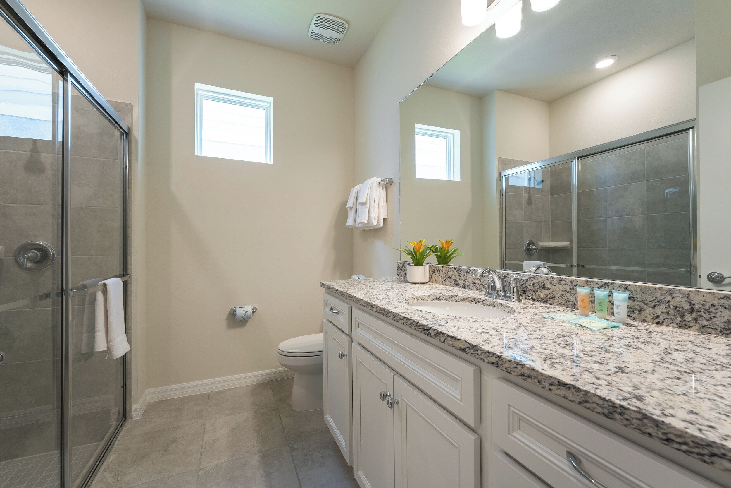 A modern bathroom with a glass shower enclosure, a large mirror, and a granite countertop with toiletries.
