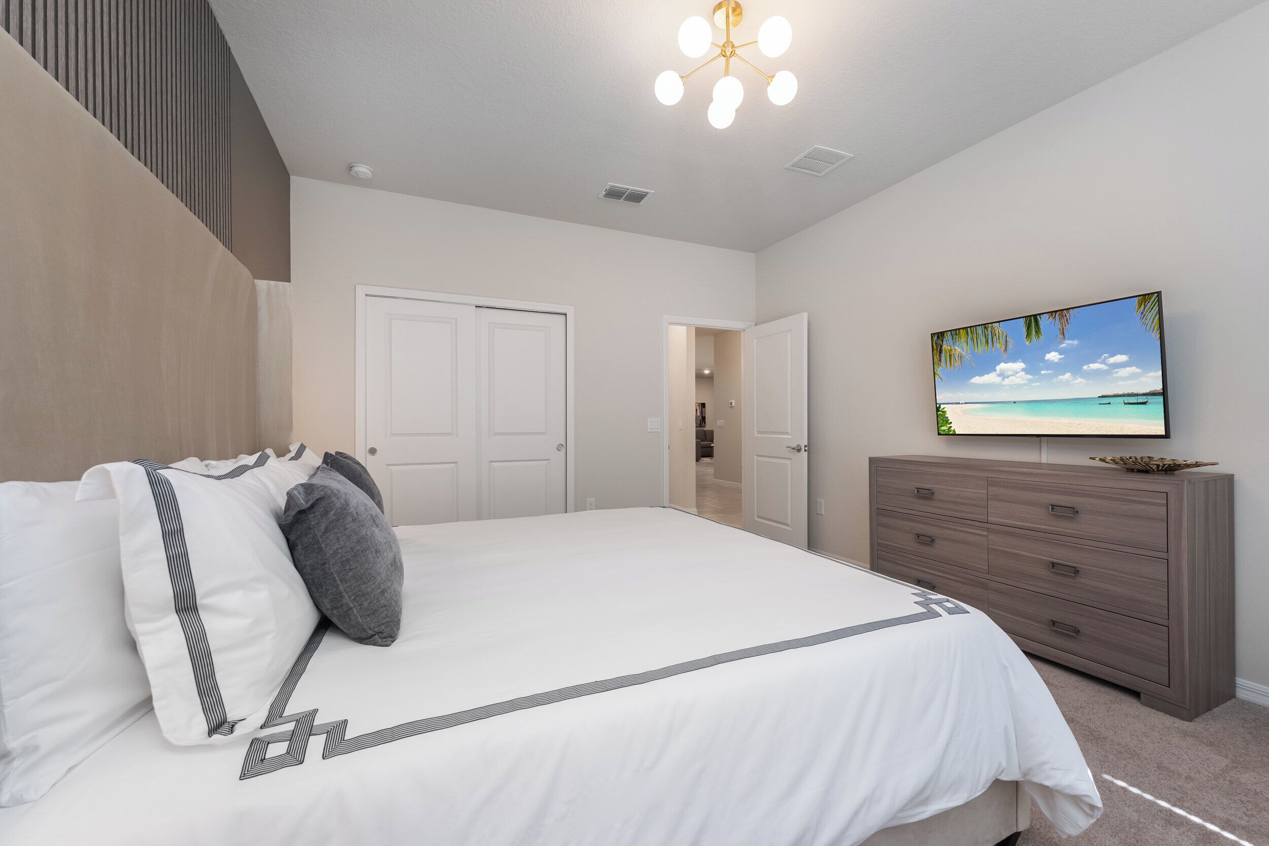 Une chambre à coucher comprenant un lit, une commode, un téléviseur et une porte donnant sur une autre pièce.