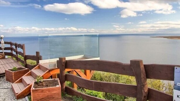 Une terrasse en bois dotée de jardinières intégrées et d’une balustrade en verre, offrant une vue sur une étendue d’eau paisible.