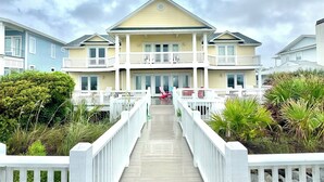 A two-story building with a central balcony, a wooden deck leading to the entrance, and surrounding greenery. - Oceanfront w/ sandy beach all day! 4100sq ft. Retreat w/ Private walk, Pet’s ok! (Fripp Island)