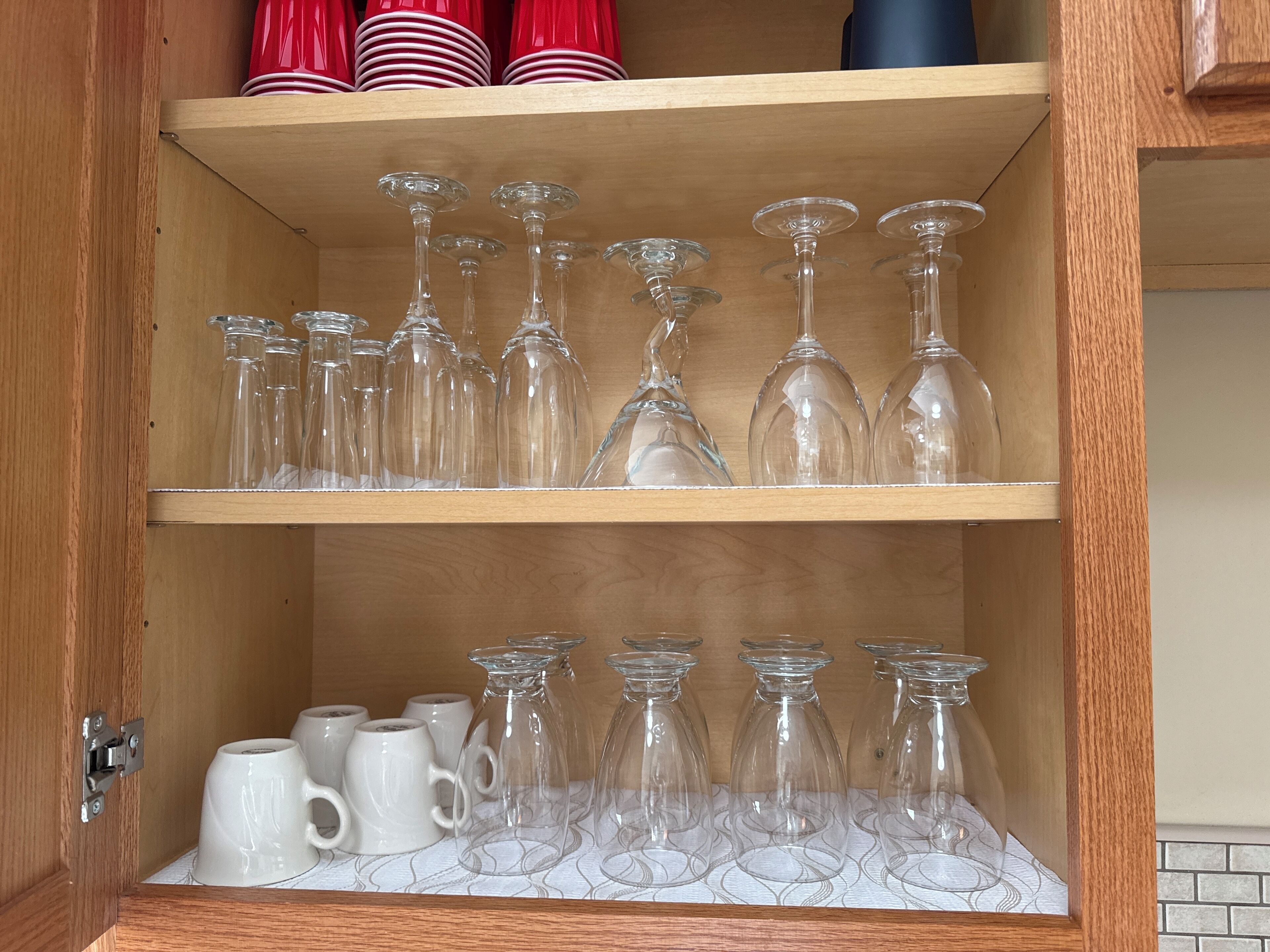 Et træskab med hylder, der indeholder forskelligt glas, herunder vinglas og krus.