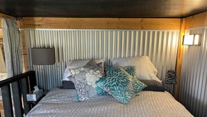 Una cama con ropa de cama estampada, almohadas, una lámpara de noche y un cabecero a rayas.