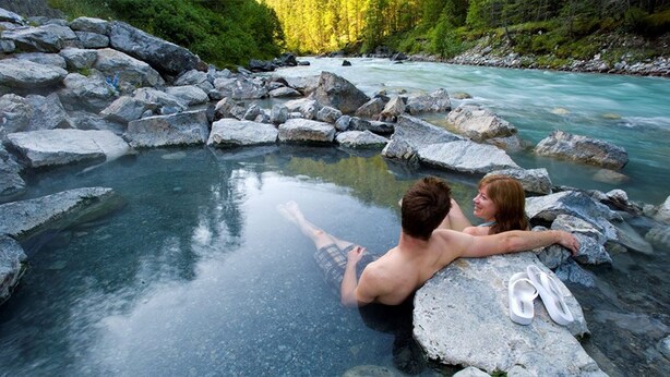 Una pareja en aguas termales, rodeada de rocas y un río.