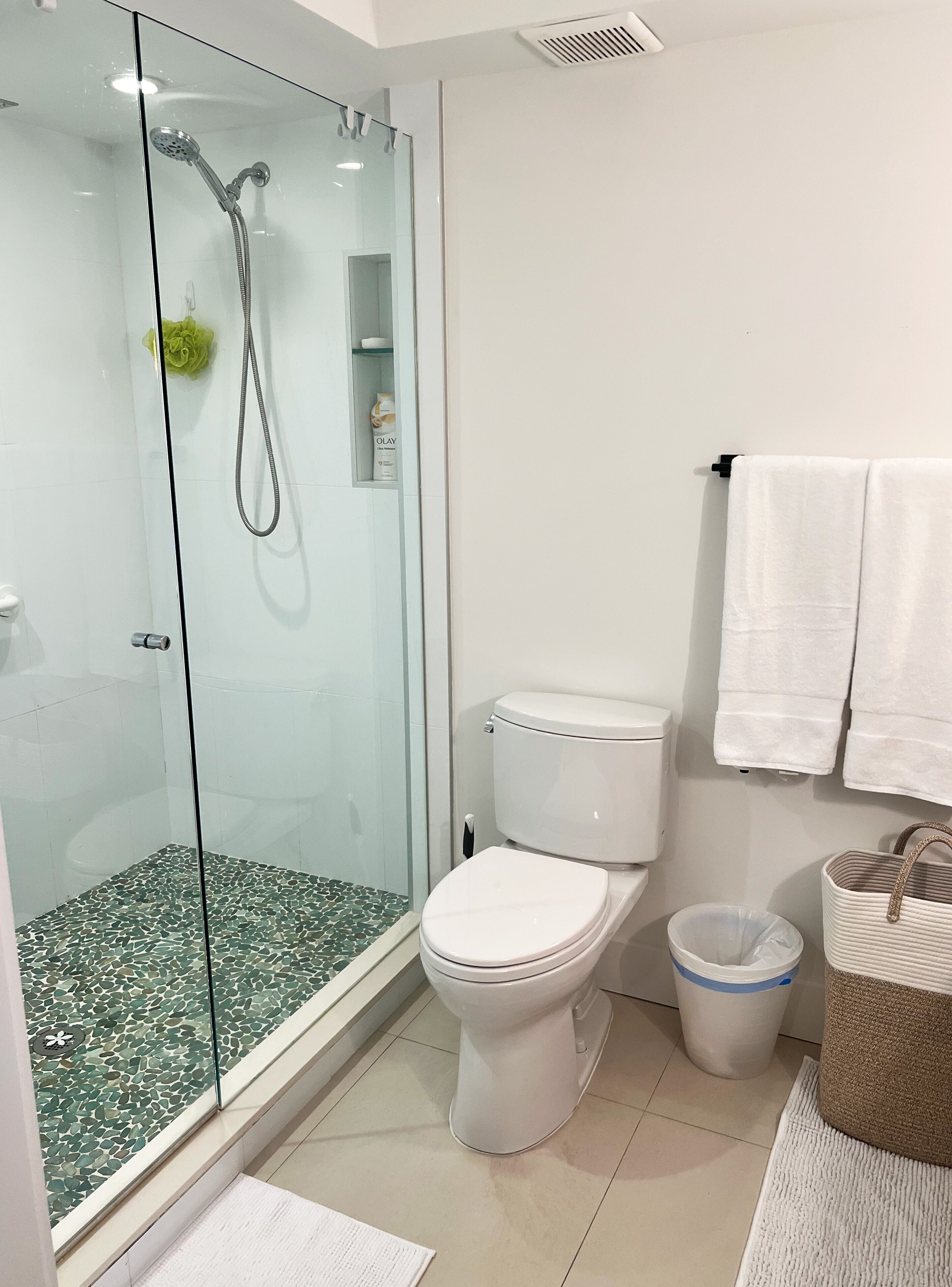 A modern bathroom with a glass-enclosed shower, a white toilet, and a trash bin.