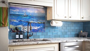 Una cocina con un salpicadero de azulejos azules, un lavabo y un cuadro de un velero en la pared.