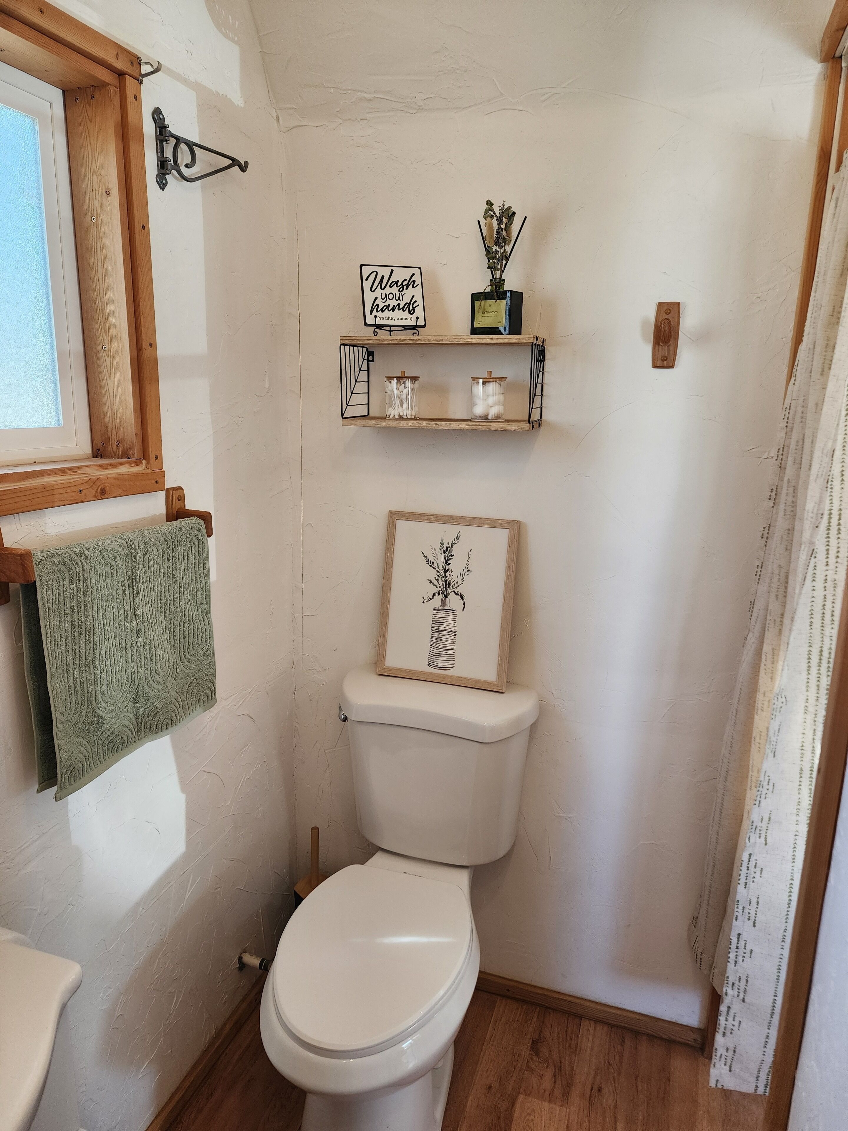 Uma casa de banho com sanita, uma estante com um quadro e uma garrafa, e uma toalha pendurada num porta-toalhas.