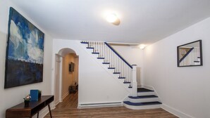 Una escalera con barandillas blancas y detalles azules, piso de madera y un cuadro en la pared.