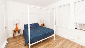 Un dormitorio con cama de dos plazas, paredes blancas, suelo de madera y ventana con persianas.