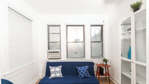 Una habitación con un sofá azul, dos almohadones estampados, una mesita de madera y un estante blanco.