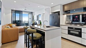 Una cocina moderna con una isla central, taburetes de bar, horno empotrado y un área de comedor con sofá y sillas.