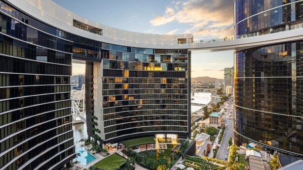 Un edificio moderno con fachada de vidrio curva, piscina en la azotea y un puente peatonal.