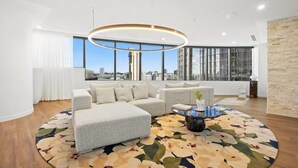 Una sala de estar moderna con un sofá, una mesa de centro redonda y vistas de la ciudad a través de grandes ventanales.
