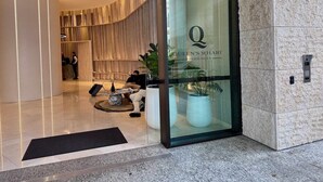 A modern hotel entrance with a glass door displaying "Queen's Wharf Residences" and a reception area with a seating area and a reception desk.