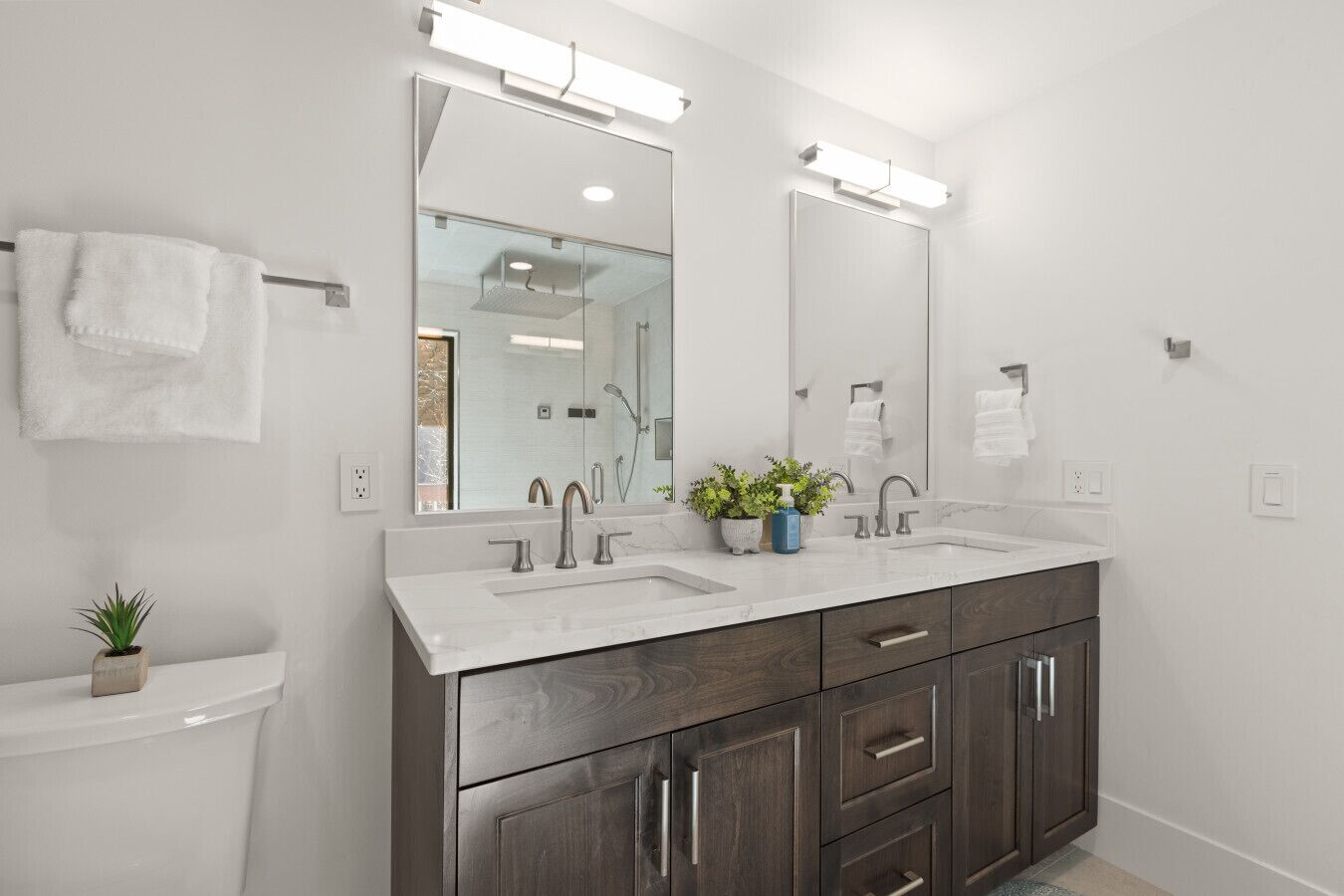 Une salle de bain moderne avec deux vasques, des meubles en bois foncé et un grand miroir.