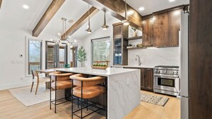 Une cuisine moderne dotée d’un grand îlot central, de tabourets de bar, de poutres en bois et d’appareils électroménagers en acier inoxydable.