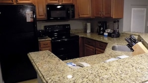 Una cocina con gabinetes de madera, un refrigerador negro, un microondas, una estufa y encimeras de granito.