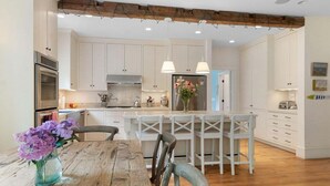 Une cuisine avec des meubles blancs, une table en bois et un luminaire suspendu.