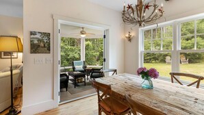 Un espace repas comprenant une table et des chaises en bois, un lustre et une vue sur l’extérieur.