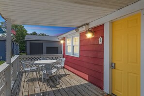 A covered porch with a table and chairs, a yellow door, and a red wall with a number sign. - NEW! Dave's Last Resort Poolside - Long Stay Discount - Relaxing Cabin 3 (Monticello)