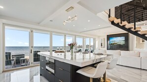 A modern kitchen with a large island, a dining area, and a view of the sea. - Brand New Home Ocean Views Wolf Appliances (Wells)